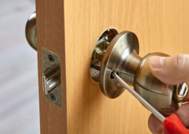 Installer fixes door knob with lock using screwdriver.